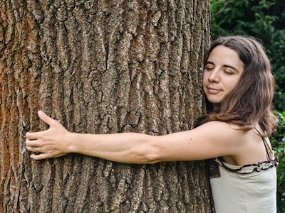 Eine Frau mit geschlossenen Augen umarmt einen Baum. Das Thema des Fotos ist 'der Natur zuhören'